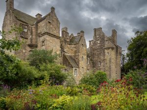 Hige old castle surrounded by bright shrubs and flowers set against a moody sky.