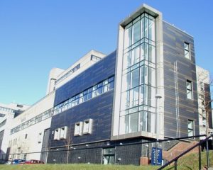 External shot of the SCAPA building. This is a modern, tall, tile and glass clad building framed by a clear blue sky.